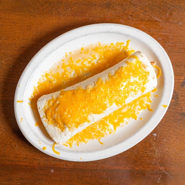 A cheese-covered burrito on a white oval plate, centered on a rustic wooden table.