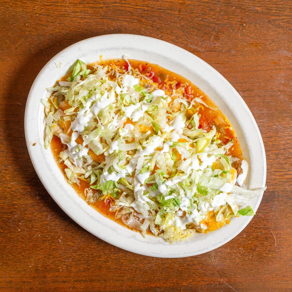A white oval plate holds a Mexican dish topped with shredded lettuce, sour cream, and red sauce.