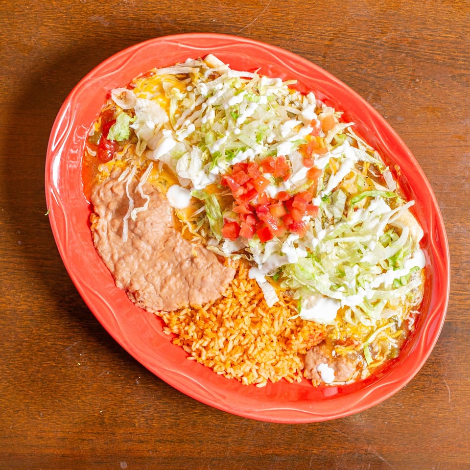 A vibrant red plate filled with Mexican food, including rice, beans, and enchiladas topped with lettuce, tomatoes, and sour cream.