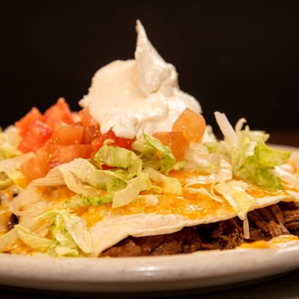 Shredded beef enchilada topped with melted cheese, lettuce, diced tomatoes, and a dollop of sour cream.