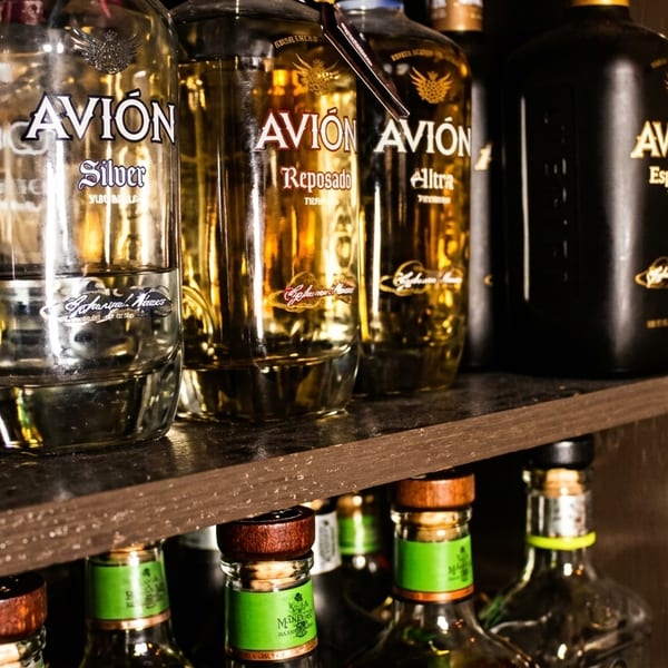 Bottles of Avion tequila, including Silver, Reposado, Ultra, and Espresso, displayed on wooden shelves.