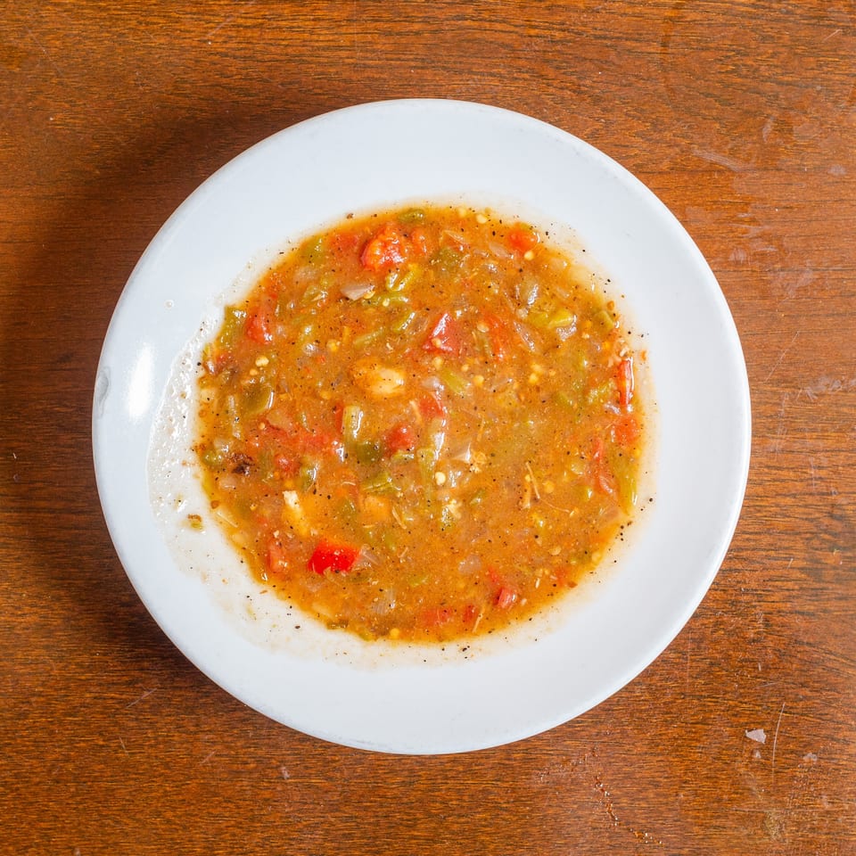 A white plate filled with chunky salsa, featuring visible tomatoes, onions, and green peppers, on a wooden table.