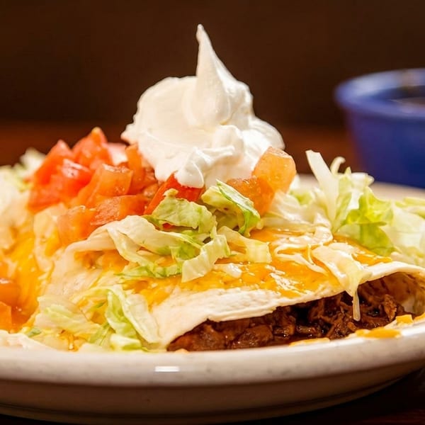 Beef enchilada topped with shredded lettuce, diced tomatoes, cheese, and a dollop of sour cream.