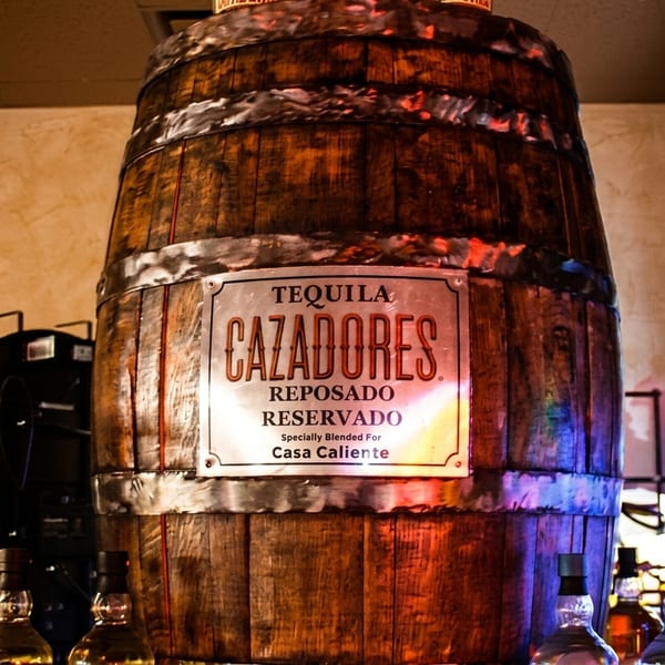 Large wooden tequila barrel with a Cazadores Tequila sign, surrounded by neon lights and bottles.