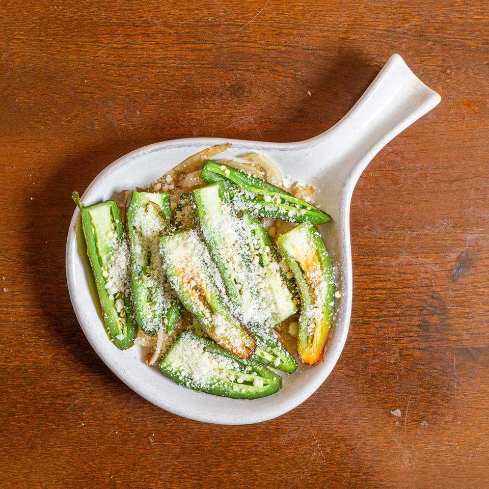Roasted green jalapeno peppers with white cheese and caramelized onions in a white dish.