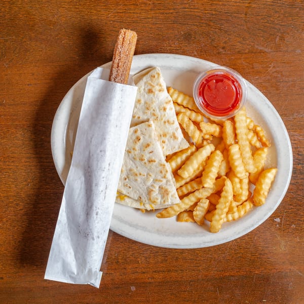 A plate with a churro in paper, cheese quesadilla slices, crinkle-cut fries, and ketchup on a wooden table.
