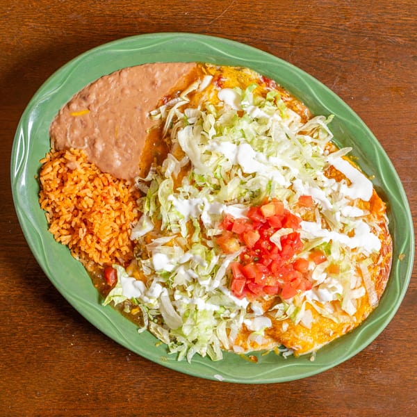 Mexican combination plate with enchiladas, rice, and refried beans, topped with lettuce, tomato, and sour cream.