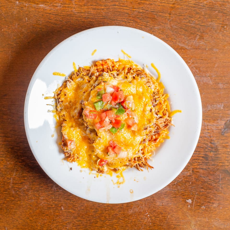 A white plate holds a cheesy chicken dish topped with diced tomatoes and green peppers.