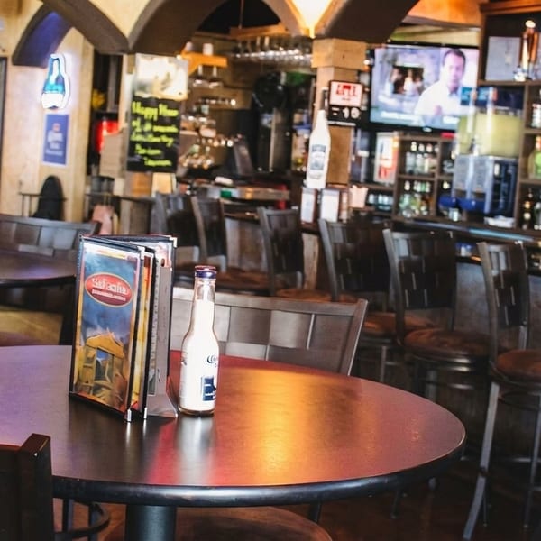 Interior of a restaurant with empty tables, chairs, and a fully stocked bar area with a TV.