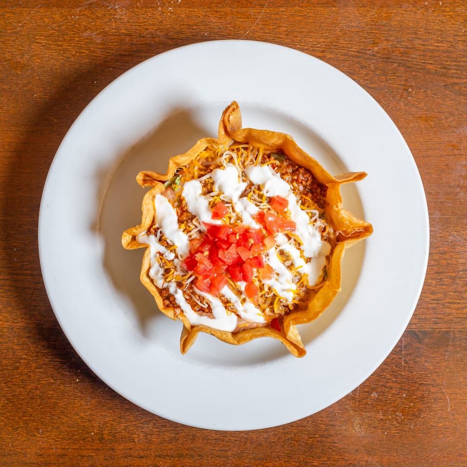 Taco salad in a crispy tortilla bowl, topped with ground beef, cheese, sour cream, and diced tomatoes.