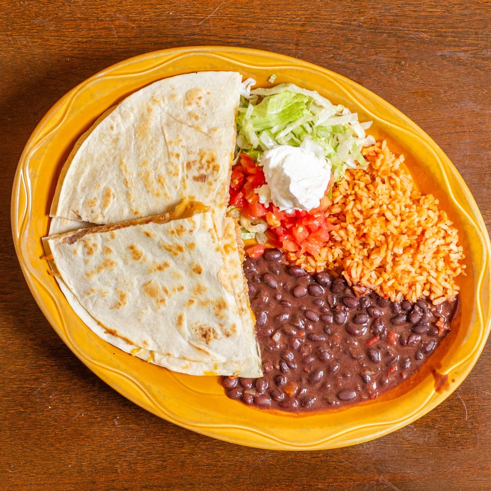 A quesadilla with rice, black beans, lettuce, tomatoes, and sour cream on a yellow plate.