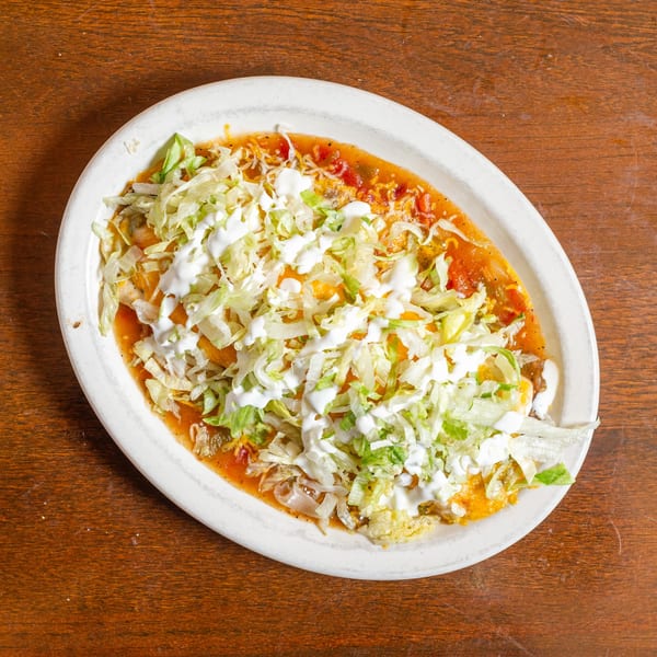 A large oval plate of enchiladas covered in red sauce, cheese, shredded lettuce, and sour cream.