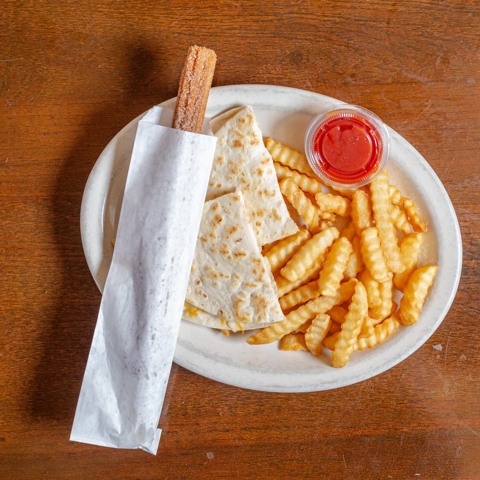 A plate with a churro in paper, quesadilla slices, crinkle-cut fries, and a side of ketchup.