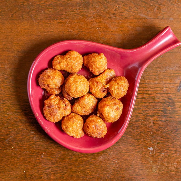 Golden-brown fried hushpuppies are served in a red, leaf-shaped dish on a wooden table.