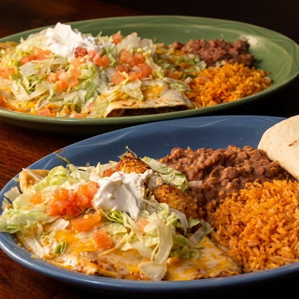 Two plates of Mexican food with enchiladas, rice, beans, and tortillas on a wooden table.