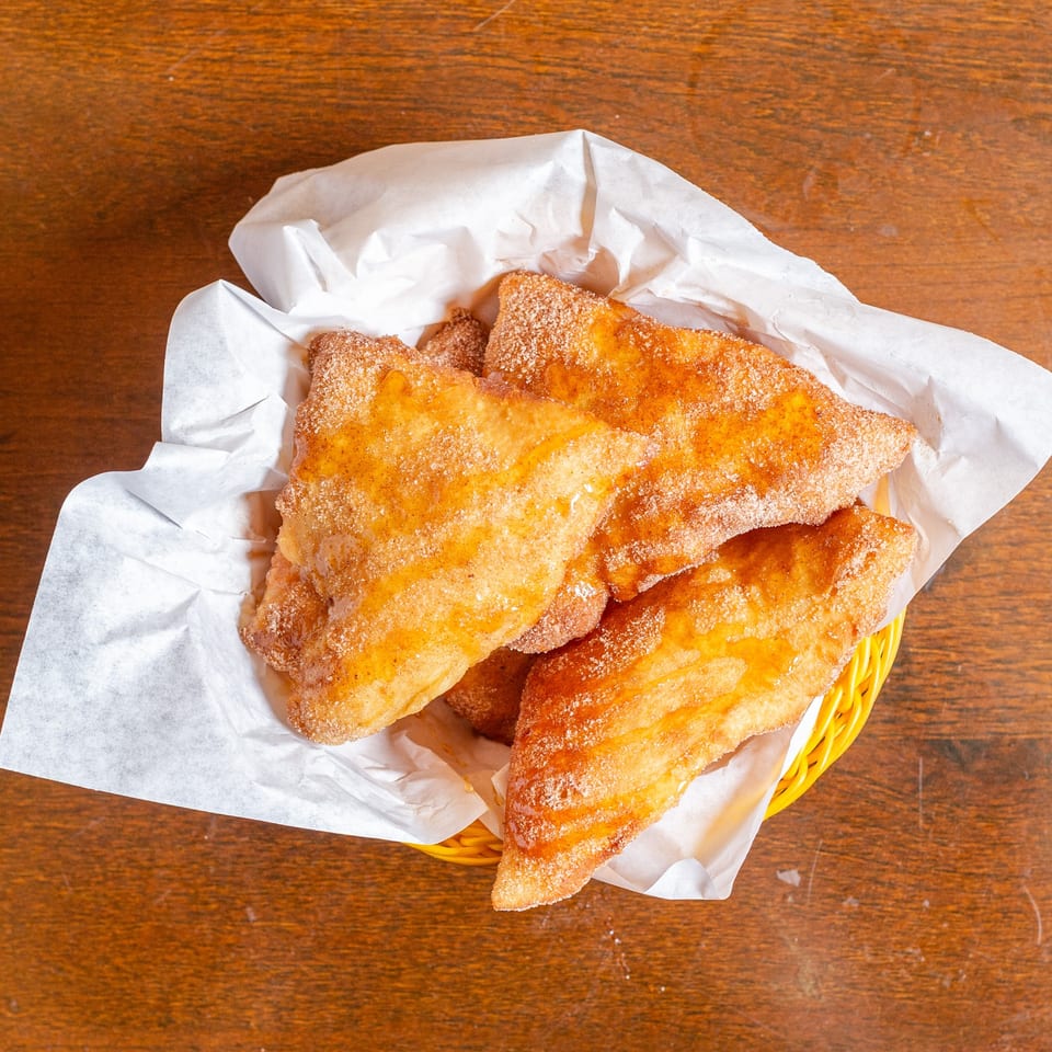 Golden brown fried pastries, drizzled with honey and sprinkled with cinnamon sugar, in a basket.
