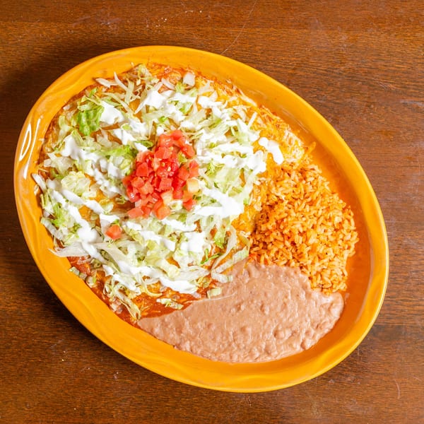 A large orange platter with a burrito covered in lettuce, sour cream, and diced tomatoes, alongside rice and refried beans.